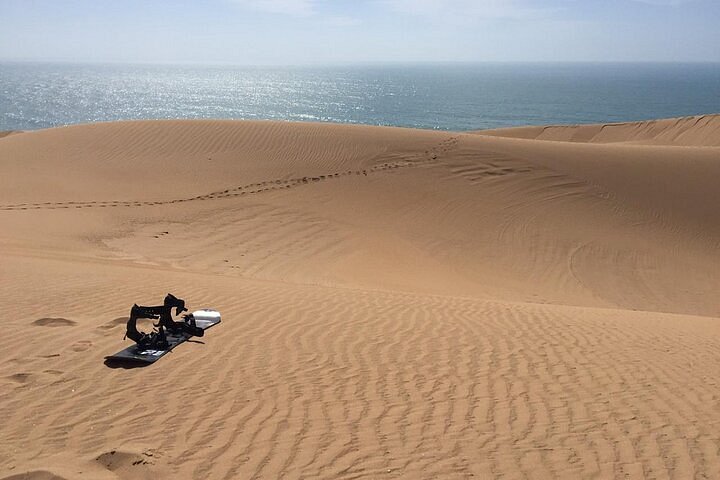 Traveler sandboarding down a steep dune at Timlalin with the Atlantic Ocean in the background